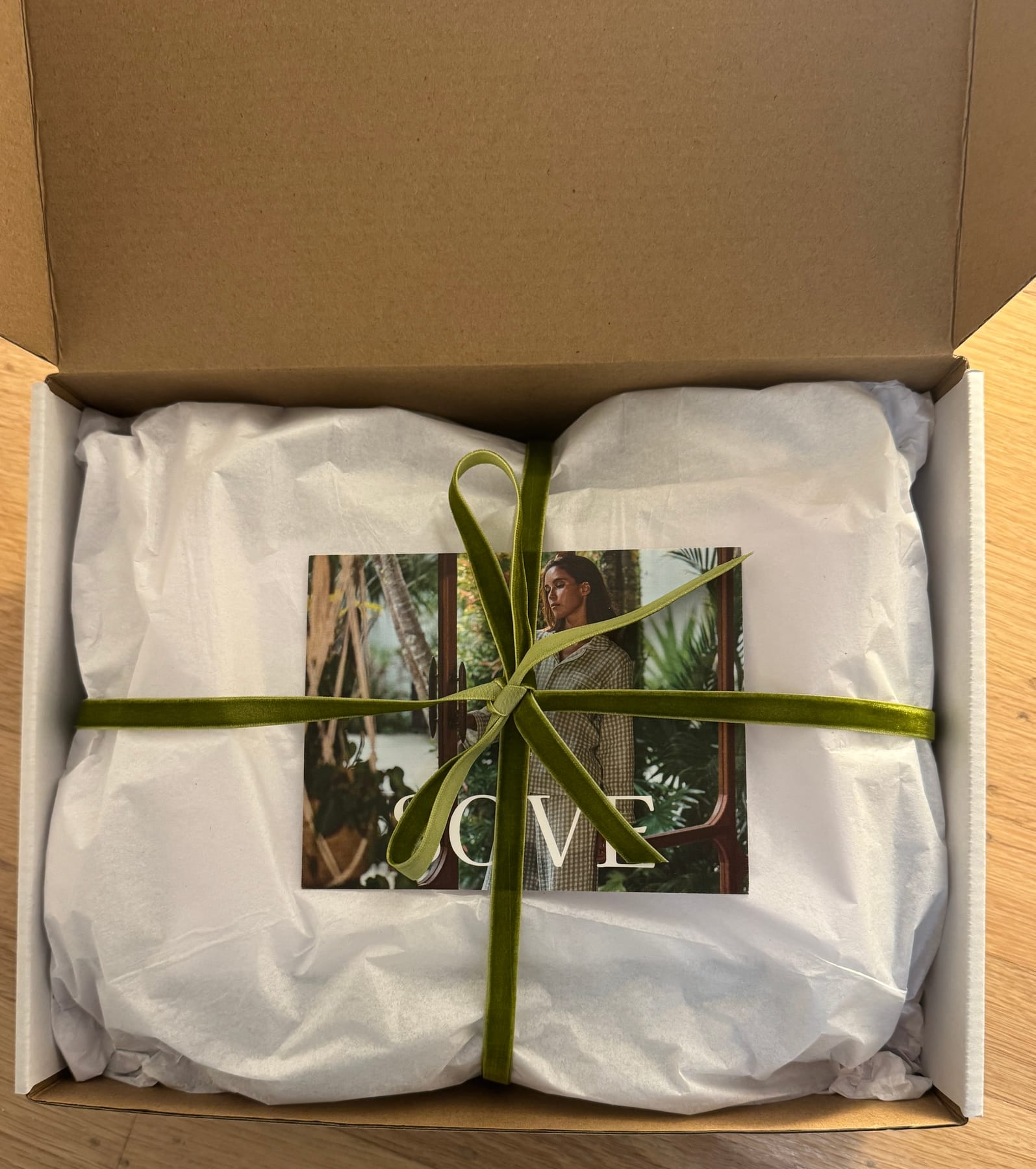 Sove packaging box with tissue paper, a green ribbon, and a campaign card